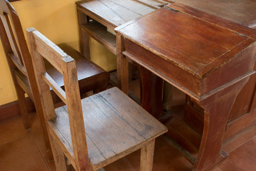 Old classroom with wood desk and chair on dark floor with light from windows.