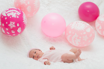 Новорожденный лежит на белом пледе с воздушными шариками