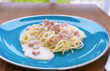 Spaghetti Carbonara with bacon and cheese in a blue plate on a wooden table.