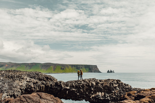 Couple standing on natural arch by sea