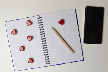 Open notebook with red hearts and mobile phone on white background. Top view