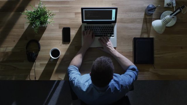 Top View of Male Programmer Writing Code on His Desktop Computer at Night. His Table is Illuminated by Cold Blue Light From Outside.  Shot on RED Cinema Camera in 4K (UHD).
