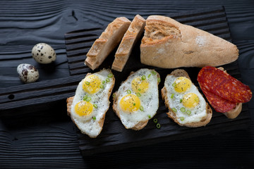 Sliced baguette with fried quail eggs on a black serving board