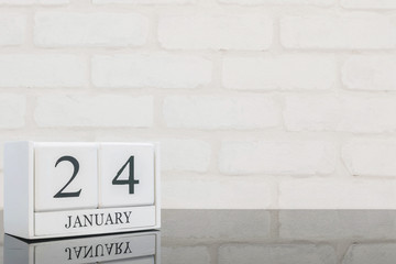 Closeup white wooden calendar with black 24 january word on black glass table and white brick wall textured background with copy space , selective focus at the calendar