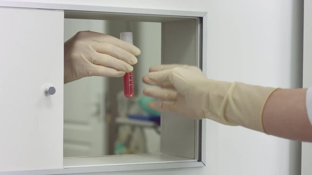 Assistant pass hand to hand liquid pink sample in test tube from surgery to laboratory