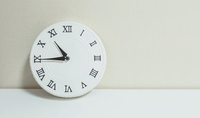 Closeup white clock for decorate show a quarter to eleven or 10:45 a.m. on white wood desk and cream wallpaper textured background with copy space