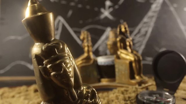 Pharaoh Statues on a sand video. Video of a golden pharaoh statues with sand and compass laying on archeology table with black board drawn pyramids on a background.