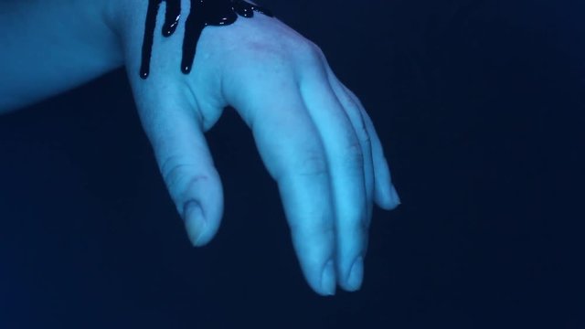 Close-up video of a thick blood flowing down a female hand in blue lights.