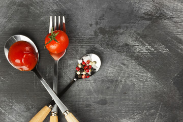 Tomato sauce, cherry, spices in fork and spoons on a dark backgr