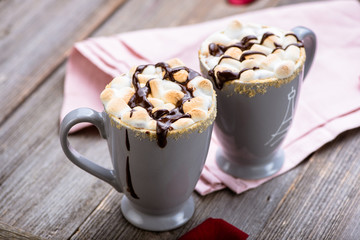 S'mores drink. Two mugs of hot chocolate with marshmallows on a wooden table. Cocoa. Rose petals. Valentine.