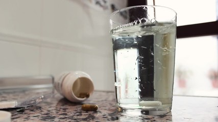 Hand throwing a tablet in glass with water and stir