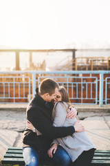 People in love theme. Attractive young couple dating and enjoying in urban city outdoors. They sitting on the bench, hugging, smiling and kissing.