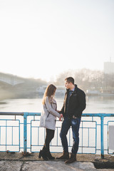 People in love theme. Attractive young couple enjoying in city outdoors. They standing on the city bridge, smiling and holding hands.