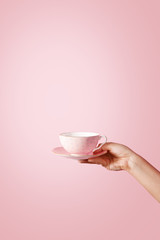 Woman hand holding a teacup on pastel background