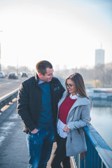 People in love theme. Attractive young couple enjoying in city outdoors. They standing on the city bridge, smiling and hugging.