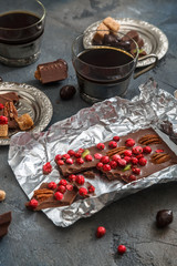 Chocolate bar with berries and nuts in foil on dark background