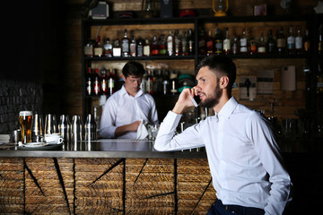 Man in white shirt speaking by cellphone near wooden bar counter