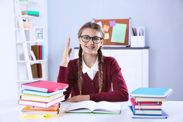 Teenage girl with pile of books sitting at desk in a classroom