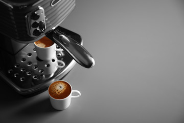 New coffee machine and two cups with fresh espresso on grey background