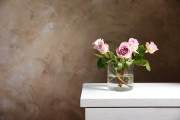 Glass vase with bouquet of beautiful roses on color background