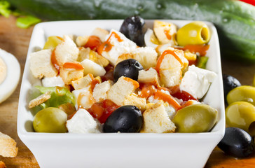 Simple, fresh salad with vegetables, olives and cheese in white bowl on a wooden board.