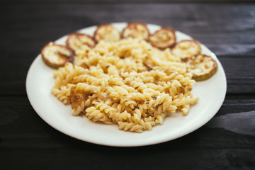 Pasta with fried zucchini on the plate on wooden background.