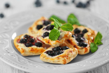 Sweet tasty pastries and fresh bilberries on plate against wooden background, closeup