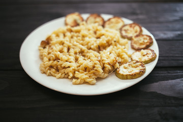 Pasta with fried zucchini on the plate on wooden background.