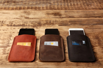 Leather cases with mobile phones and credit cards on wooden background