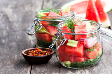 Marinated  watermelon with herbs in a glass jar on wooden table