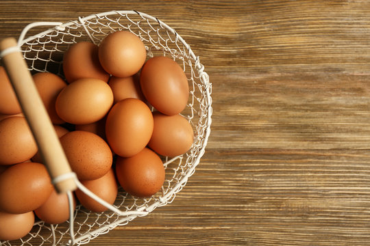 Raw eggs in basket on wooden background