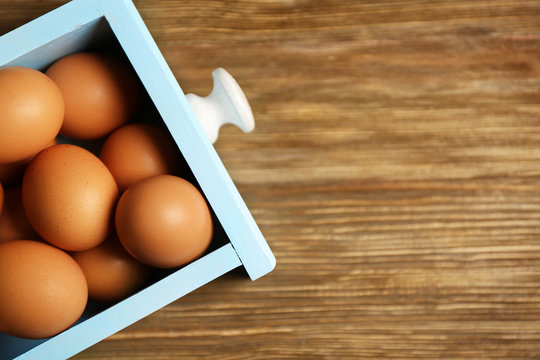 Raw eggs in drawer on wooden background
