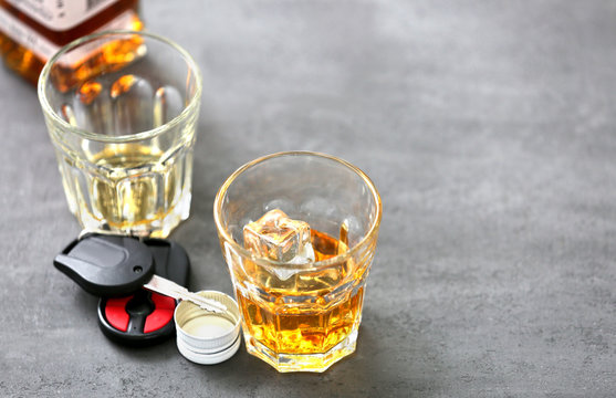 Glass with alcohol and car keys on grey background