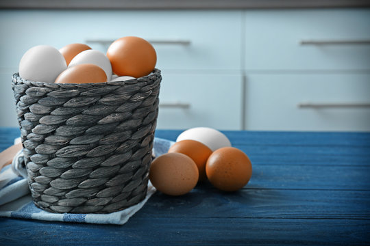 Wicker basket with raw eggs on wooden table