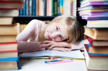 Cute little girl lying on table while doing her homework.