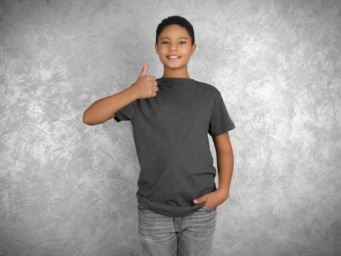Young African American boy in blank gray t-shirt standing against textured wall