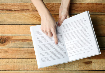 Naklejka premium Female hands holding opened book on wooden background