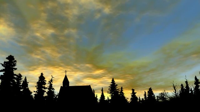 Sunset golden clouds over a silhouette church with trees 