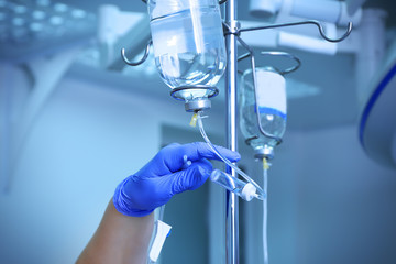 Doctor's hand and infusion drip in hospital on blurred background