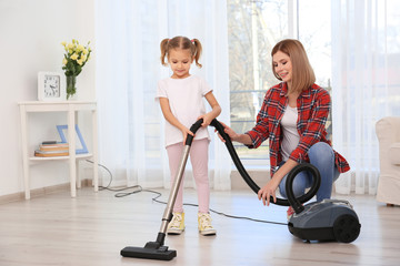 Pretty woman and her daughter hoovering floor at home