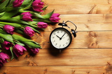 Purple beautiful tulips with alarm clock on wooden background