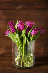 Glass vase with bouquet of beautiful tulips on wooden background