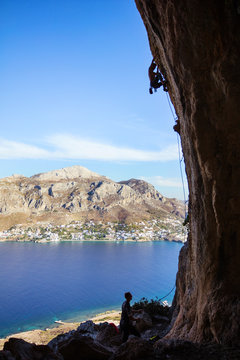 Young man climbing on overhanging cliff, his partner belaying. Telondos Island, Greece. 