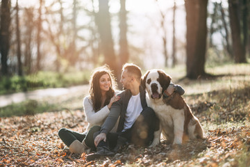 Young couple enjoying nature outdoors together with their adorable Saint Bernard puppy. People and dogs theme.
