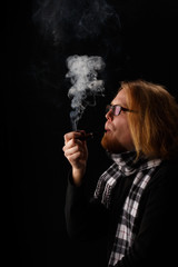 Obraz premium Man with red beard in chequered scarf and glasses holds tobacco