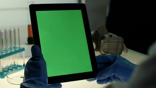 Scientist using tablet PC with green screen in modern laboratory on a background of test tubes and protective mask