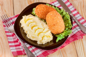 two fried breaded cutlet with mashed potatoes and lettuce on a black plate wooden background