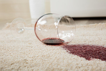 Rotwein aus Glas auf Teppich verschüttet