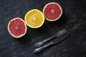 grey fruit and orange sitting on top of the dark wooden table together with an old silver fork and knife.