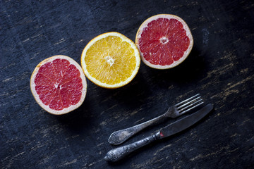 grey fruit and orange sitting on top of the dark wooden table together with an old silver fork and knife.